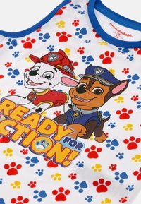 Canotta bianca con cani dei cartoni animati colorati, bordi blu e scritta "PRONTO PER L'AZIONE!", con un motivo di impronte di zampe in rosso, blu e giallo.