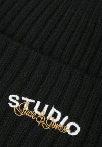 Sort strikket hue med ribbet tekstur. Viser "STUDIO Jack & Jones" broderet med hvid og gylden tråd.