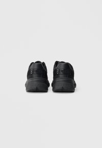 Ζευγάρι μαύρα αθλητικά παπούτσια Guess, εμφανιζόμενα από πίσω, με παχιές σόλες και λουράκια με το λογότυπο στη φτέρνα, σε απλό αχνό φόντο.