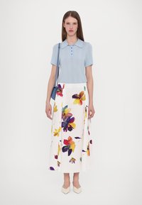 Lichtblauwe polo met korte mouwen en verticale strepen, gecombineerd met een witte midi-jurk met een meerkleurig bloemenpatroon. Vierkante schoenen.