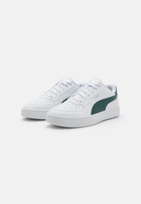 Hvide sneakers med en glat læderoverdel, perforeret tå for åndbarhed og grøn ruskindslateralaccent. Tykk hvid gummisål.