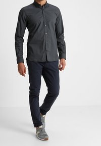Donkergrijze overhemd met lange mouwen en een subtiel patroon, gecombineerd met marineblauwe chinos en grijze sneakers met beige accenten.