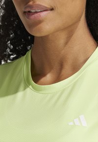 Svetlozelené športové tričko s textúrovanou tkaninou a okrúhlym výstrihom, s bielym logom Adidas na hrudi.