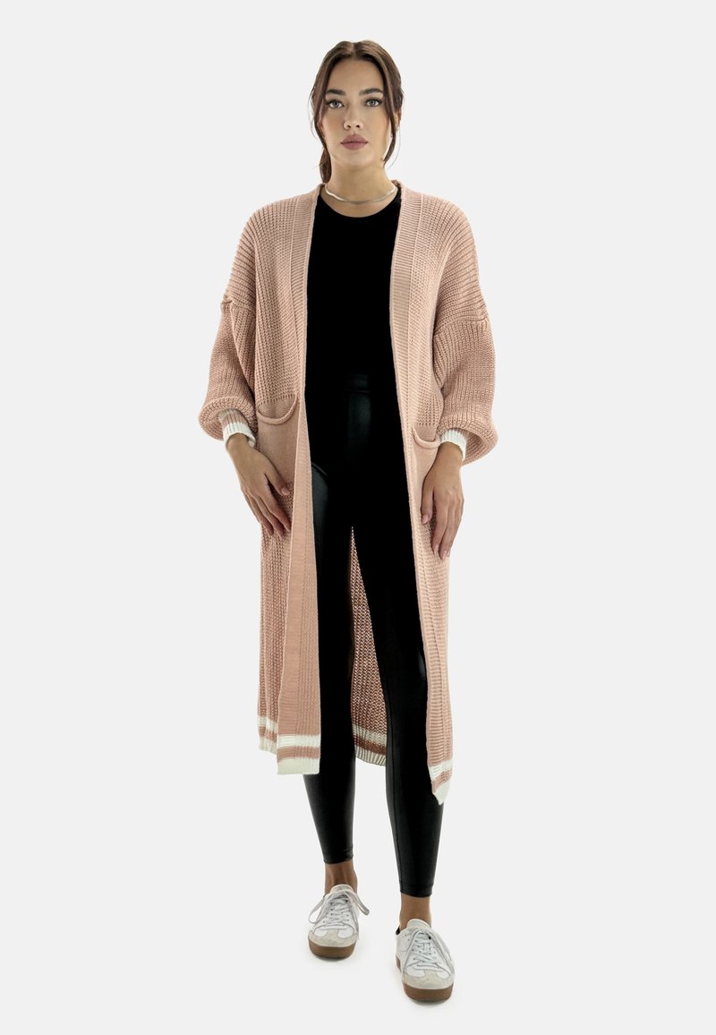 Lång, öppen cardigan i mjuk rosa med ribbat mönster, två fickor och krämfärgade detaljer vid ärmsluten och fållen. Bärs över svarta leggings.