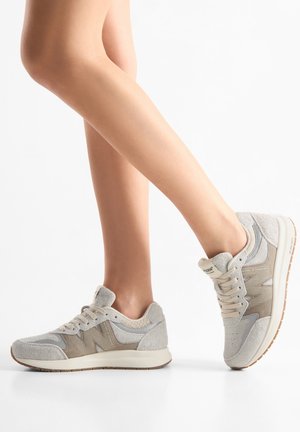 Lichtgrijze sportschoenen gemaakt van suède en mesh, met een textuur op het oppervlak, veters en een witte zool met een bodem van gumrubber.