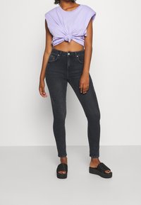 Fialové zkrácené tričko s uzlovým detailem, spárované s vysokými tmavě šedými úzkými džíny a černými platformovými sandály s žebrovanými akcenty.