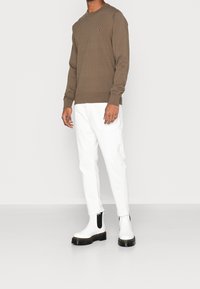 Bruine trui met lange mouwen en een ronde hals, gecombineerd met witte slimfitbroek. Schoenen zijn witte Chelsea laarzen met zwarte accenten en een dikke zool.