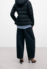Svart puffjacka med huva, försedd med kviltat mönster. Matchas med lösa mörka denim byxor med vida ben och svarta högklackade sandaler.