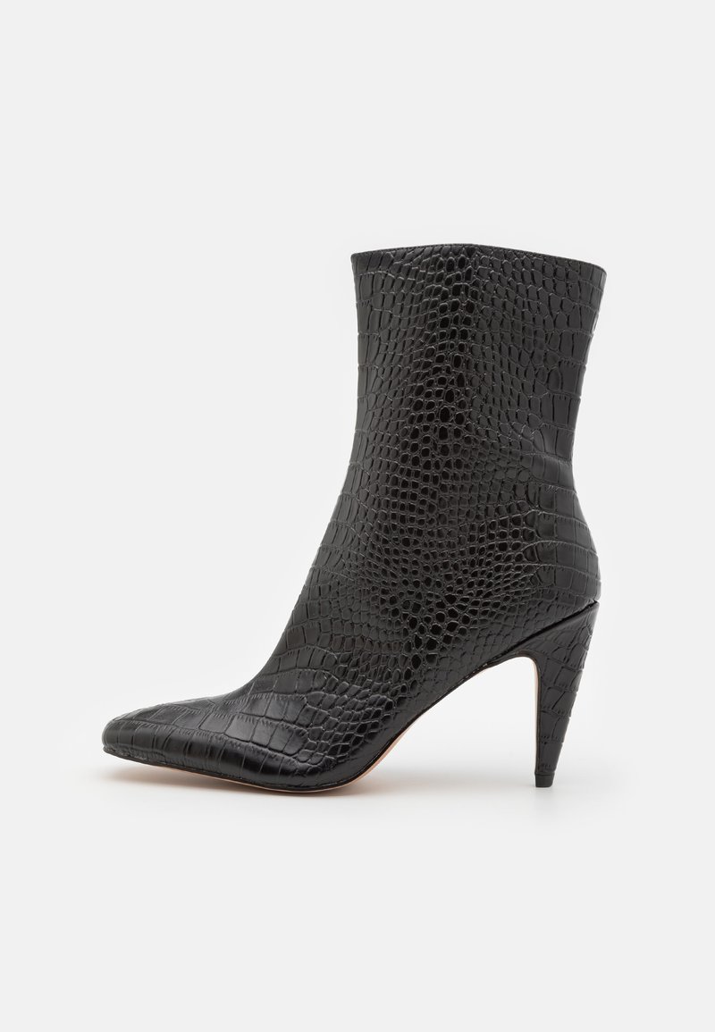 Bottine noire à bout pointu, motif crocodile texturé, et talon effilé de hauteur moyenne sur fond blanc.
