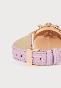 Orologio color oro rose con cinturino in pelle con stampa coccodrillo di colore viola e fibbia, caratterizzato da un accento di cristallo e una marcatura di resistenza all'acqua fino a 50 metri.