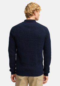 Granatowy sweter z prążkowanego materiału, z złożonym kołnierzem, długimi rękawami i wykończonymi mankietami. Teksturowana dzianina zapewnia przytulny wygląd i dopasowanie.