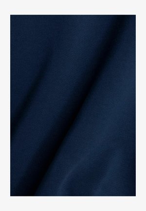 Dunkelblauer Stoff mit glatter Textur, der ein dezentes Strickmuster und sanfte Drapierungen zeigt und seine Weichheit und Flexibilität betont.