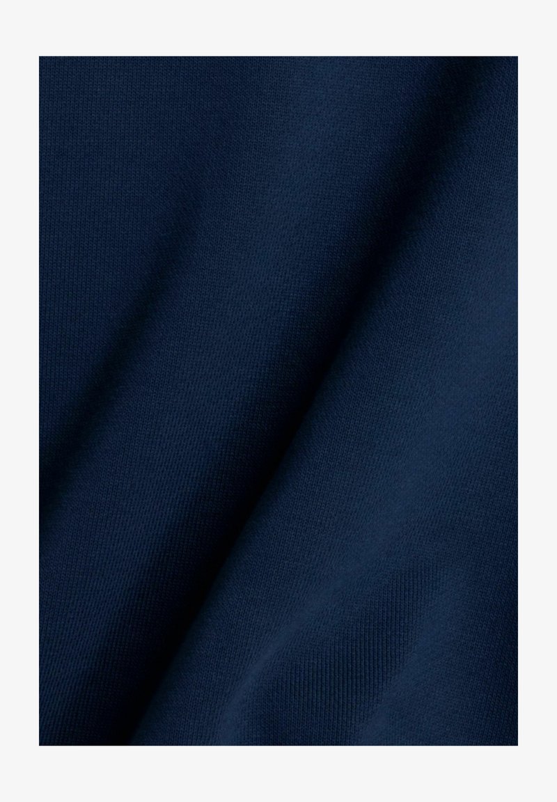 Donkerblauwe stof met een gladde textuur, met een subtiel breipatroon en zachte plooien, waarmee de zachtheid en flexibiliteit worden benadrukt.