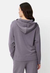 Paarse hoodie gemaakt van zachte, gladde stof. Heeft een losse pasvorm, verlaagde schouders en een grote capuchon. Eenvoudig, minimalistisch ontwerp.