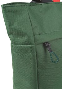 Bolsa de tela verde con una superficie texturizada, que cuenta con un bolsillo frontal y un lazo de sujeción negro con un cordón verde y blanco con puntos.