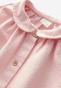 Ljusrosa randig blus med rundad krage, knappframsida och små träknappar. Mjukt, strukturerat tyg med samlade detaljer.