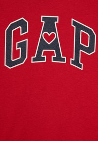 Red cotton t-shirt featuring the word "GAP" in navy letters, with a heart shape integrated into the letter "A." Soft texture.