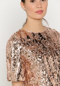 Sequin top featuring a metallic sheen in rose gold and copper tones, with a round neckline and short sleeves, highlighting a textured design.