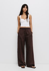 Hvid fitted crop top med twist-design; brune brede bukser med lodrette hvide striber; glat stof; elastisk talje.
