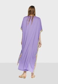 Lila kaftan i lättviktsmaterial, med färgglad blommig kant längs sidorna och en lös, flödande design.