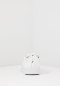 Vita sneakers med slät läderöverdel, gummisula och metalliskt logomärke på hälen. Har grå textilfoder och minimalistisk design.