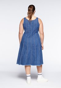 Denimklänning med en uformat knälängdssiluett, med vertikala sömnadsdetaljer, en klassisk blå färg och fransad fåll.