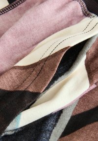 Multi-colored fabric with geometric patterns in shades of pink, brown, cream, and black; features visible stitching and varied textures.