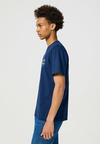 Mørkeblå bomulds t-shirt med korte ærmer, rund halsudskæring og grafisk detalje foran. Tætsiddende facon, flade sømme, blød tekstur.