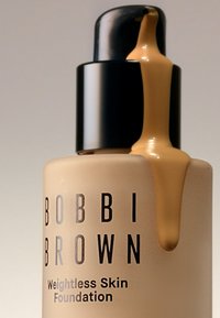 Bobbi Brown Weightless Skin Foundation i en frostet glassflaske med en svart pumpe, med en brun væske som renner fra dysen.