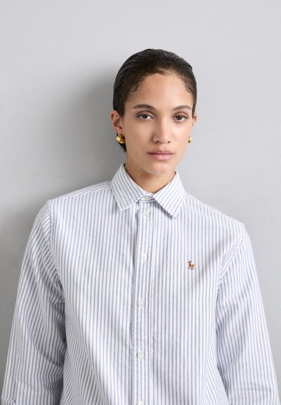Chemise à rayures bleu clair et blanche, en tissu coton, col classique, petit logo brodé sur la poitrine, boutons simples.
