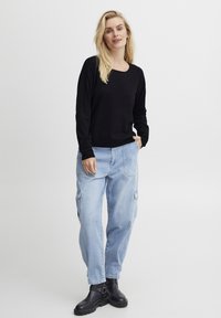 Črna dolgo rokavna pulover s svetlo modrimi cargo hlačami. Outfitu je značilna sproščena silhueta, okrogla izrezana ovratnica in črne gležnjarje.