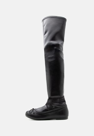 Botte plate en cuir noir haute avec bout arrondi, détail nœud et bandes élastiques autour de la cheville avec le texte "Love Moschino".