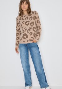 Beżowy sweter w leoparda, okrągły dekolt i długie rękawy, w połączeniu z jasnoniebieskimi spodniami o szerokich nogawkach i białymi trampkami.