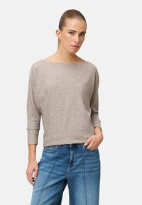 Schimmernder, hellbeiger Pullover mit weitem Bootsausschnitt, dreiviertel Ärmeln und lockerem Schnitt. Kombiniert mit blauen Denim-Jeans.