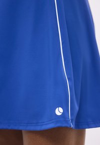 Μπλε αθλητικές βερμούδες με λευκή περιμετρική ρίγα κατά μήκος της πλευρικής ραφής και ένα μικρό λευκό κυκλικό λογότυπο κοντά στο τελείωμα.