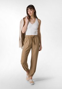 Pantalones beige estrechos con puños elásticos y cintura con cordón, combinados con una camiseta sin mangas blanca de canalé y zapatos de tela beige sin cordones.
