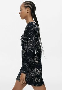 Langærmet kjole i mørkeblå stof med et blomstermotiv og abstrakt mønster i lysere nuancer. Glat tekstur med rund halsudskæring og snoretræk detalje.