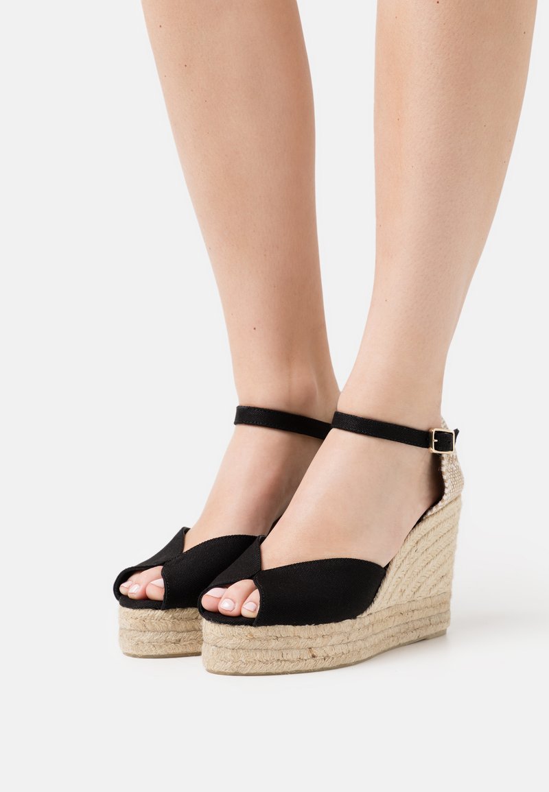 Sandali wedge neri con piattaforma in juta intrecciata, design open toe e cinturino alla caviglia regolabile. Parte superiore in tessuto liscio con motivo incrociato.