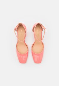 Scarpe con tacco alto in pelle sintetica rosa lucida, con punta quadrata e cinturino alla caviglia. Texture liscia, design minimalista e logo dorato "GUESS" all'interno.
