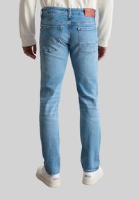 Jean en denim bleu clair avec une coupe droite, présentant une patch en cuir avec logo, deux poches arrière et un léger effet délavé sur les cuisses.