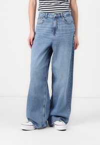Lichtblauwe, wijde jeans van denim met een hoge taille en zijzakken. Gecombineerd met witte sneakers en een gestreept shirt.