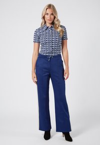 Kortärmad skjorta i navy och vit geometrisk mönster, kombinerad med högmidjade navybyxor med sidostripes och dragsko.