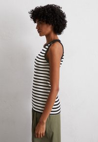 Stripet tank topp i svart og hvitt med en tettsittende design, med svarte armhull og en buet nederkant, sammen med løse olivengrønne bukser.