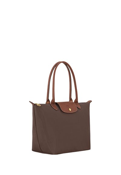 Brown tote bag with leather handles and flap closure featuring a gold button, standing upright against a white background.