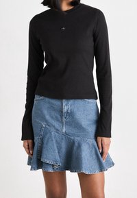 Zwarte geribbelde top met lange mouwen en een klein logo, gecombineerd met een wijde denimrok met een gerimpelde zoom en een lichte wassing.