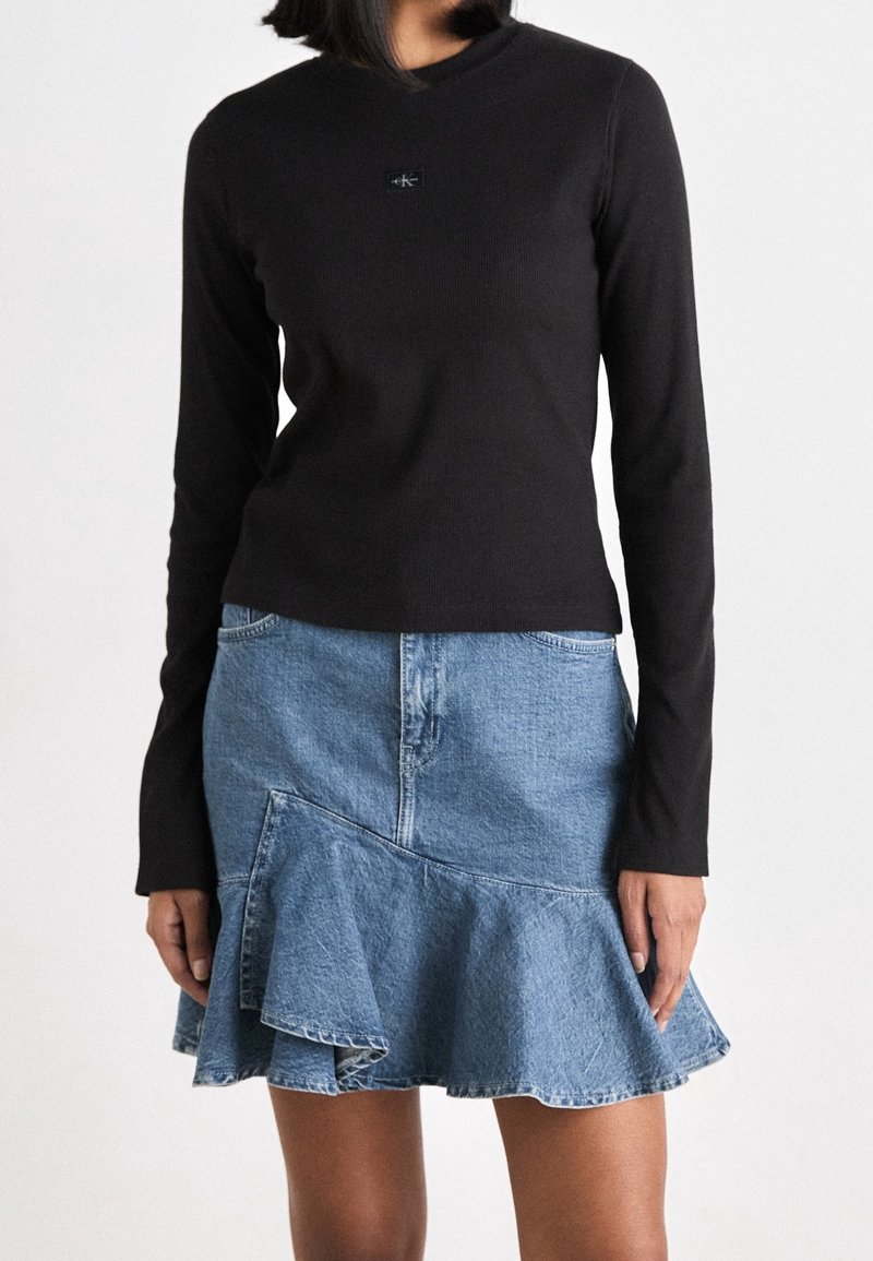 Zwarte geribbelde top met lange mouwen en een klein logo, gecombineerd met een wijde denimrok met een gerimpelde zoom en een lichte wassing.