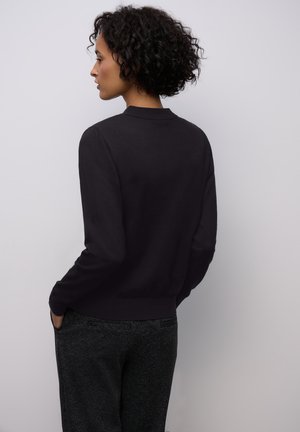 Cárdigan negro de manga larga con dobladillo y cuello acanalados, hecho de un material suave y liso; combinado con pantalones oscuros de estampado.