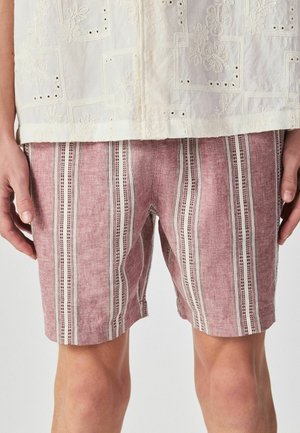 Mand iført lyserøde og hvide lodrette stribede shorts og en cremefarvet broderet skjorte med blomsterprint.