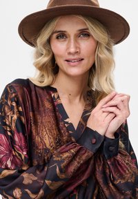 Czarna bluzka w wzory z kwiatowymi motywami w ciepłych odcieniach, z dekoltem w serek i marszczonymi rękawami, uzupełniona ciemnymi mankietami z guzikami.