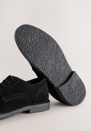 Mustast seemisnahast paeltega king, millel on tekstureeritud kummist tald, tikitud detailid ja ümar nina disain.